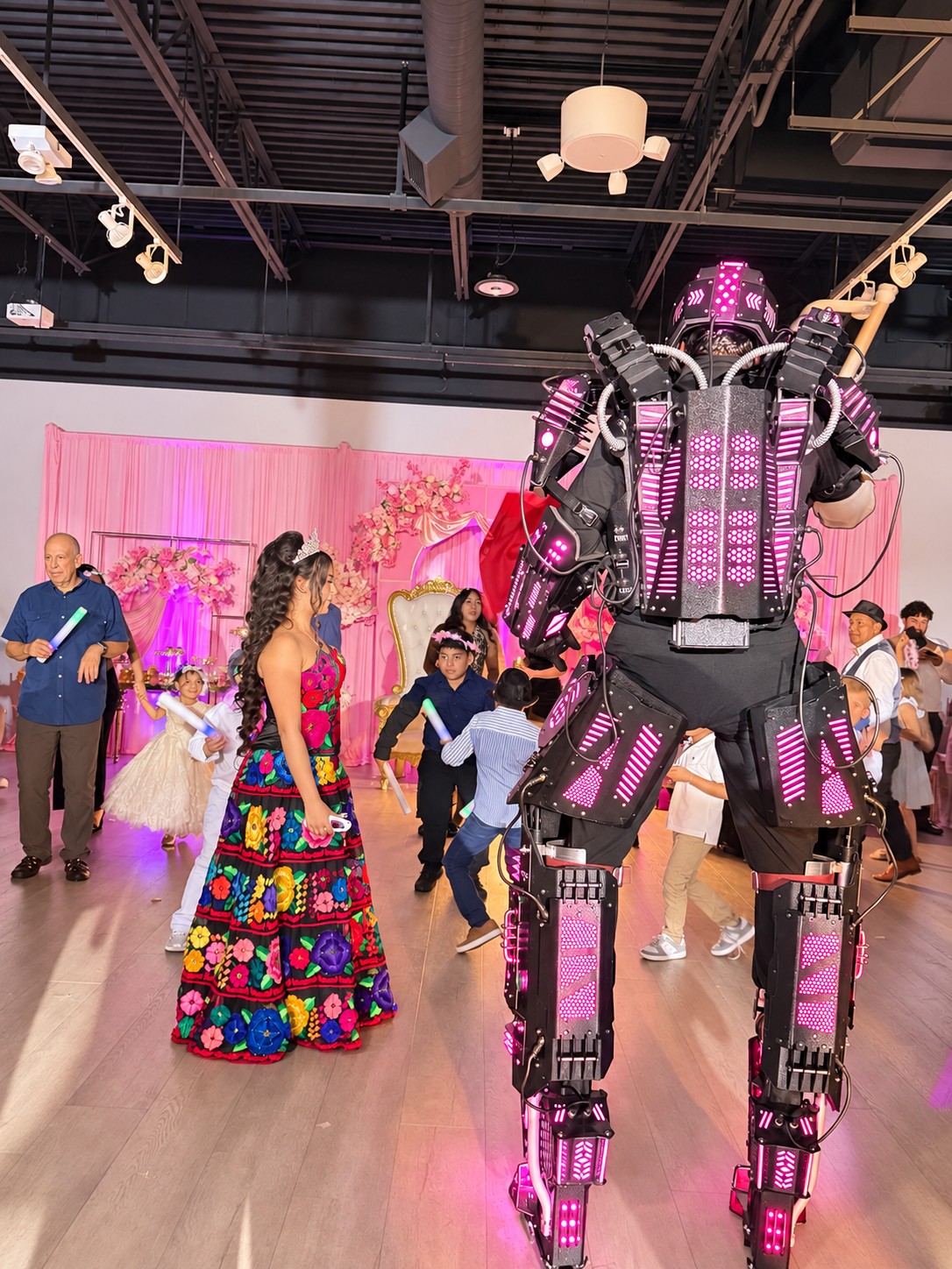 Robot iluminado en rosa animando una quinceañera junto a los invitados